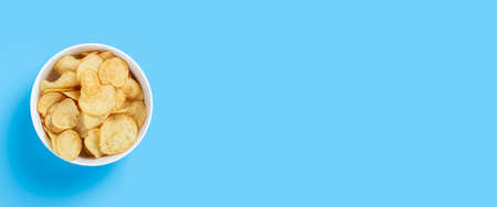 Potato chips in a bowl on a blue background. Top view, flat lay. Banner