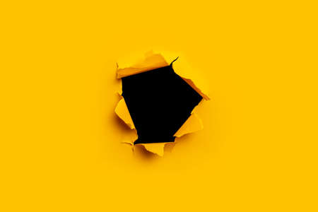 Bright yellow torn paper inside a black hole in a holeの写真素材