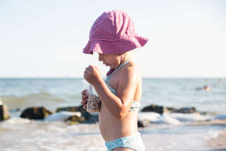 Little child girl in a swimsuit, in a Panama, plays near the sea