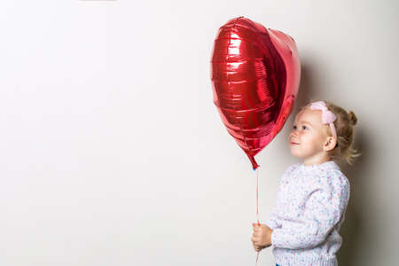 Little girl holding a heart air balloon on a light background. Concept for Valentine's Day, birthday. Banner.の写真素材