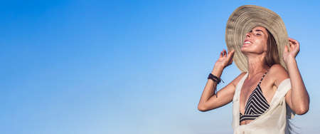 Young woman with closed eyes in a hat on a background of blue sky. Banner