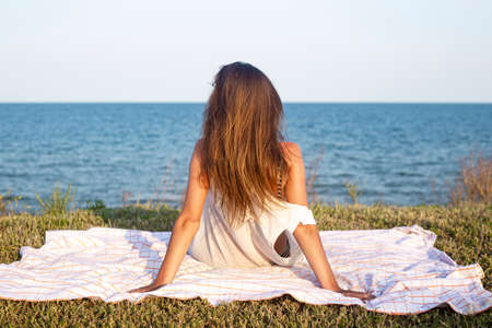 Young sexy woman sitting with her back on a cliff looking at the sea