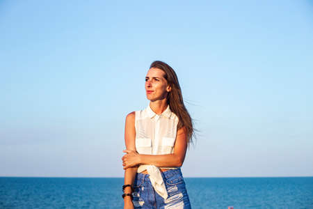 Beautiful young woman in denim shorts and shirt at the sea
