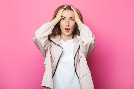 Surprised young woman in pink jacket, pink isolated background.
