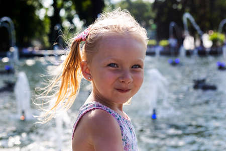 Smiling little blond child near the fountain. Real people.