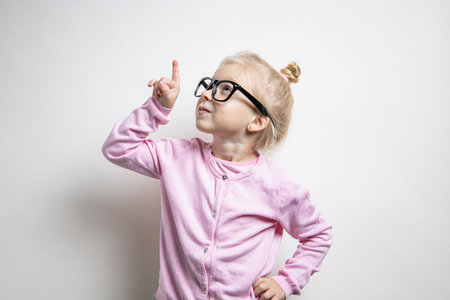 Beautiful child girl in glasses points a finger up on a light backgroundの写真素材