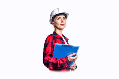 Young woman in construction clothes with clipboard on light background