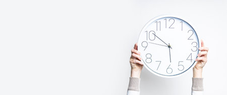 Female hands holding a large white watch on a light background. Bannerの写真素材