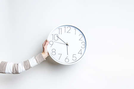 Woman's hand holds a large white clock against a light wall
