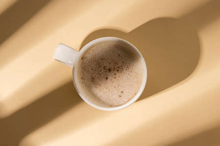 Coffee in a white cup with rays of light on a beige background. Flat lay, top viewの写真素材