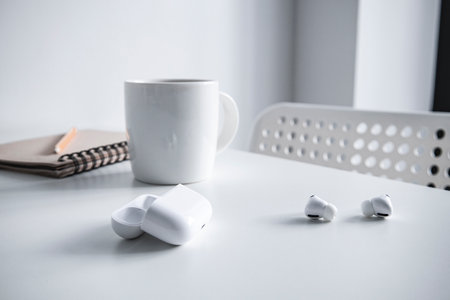 White cup with coffee, notepad, pencil and wireless headphones on a white table