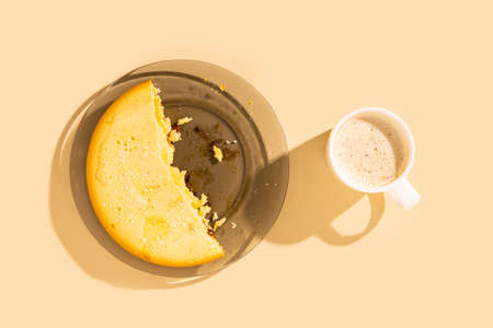 Half of a pie on a plate, a cup of cappuccino on a beige background. Top view, flat layの写真素材