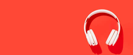 White wireless headphones on a red background. Top view, flat lay. Banner