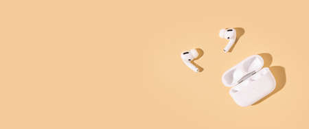 Wireless headphones on a beige background. Flat lay, top view. Banner