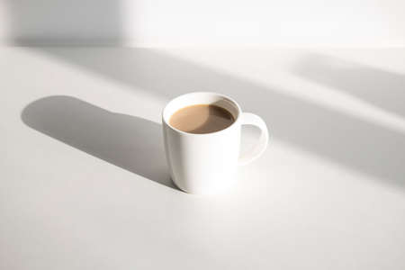 Coffee in a white cup on a white table under natural lightの写真素材