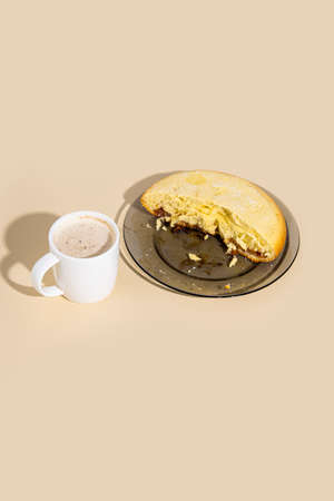 Half of a pie on a plate, a cup of cappuccino on a beige background