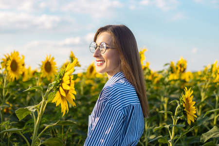 Young woman in dress and glasses enjoying the sunset on the sunflower field.の写真素材