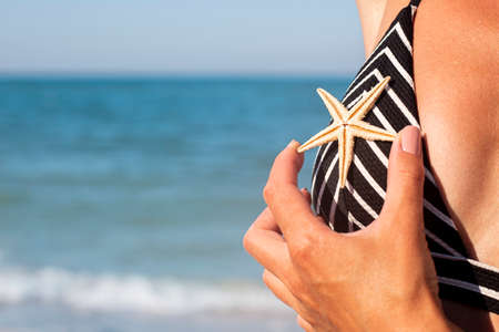 Woman on the beach in a swimsuit holding a starfish on the chest.の写真素材