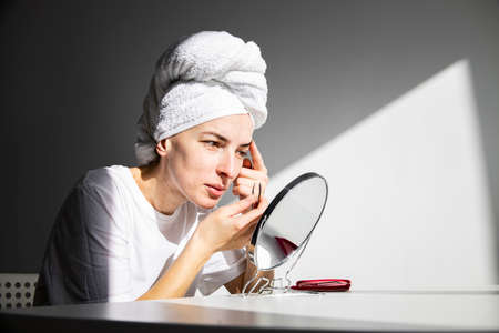 Young woman without makeup with a towel on her head makes eyebrow correction.の写真素材
