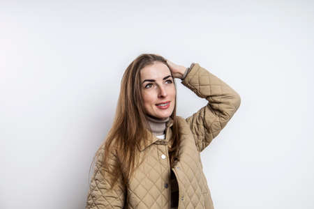 Smiling girl in a jacket straightens her hair near a white wallの写真素材
