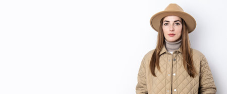Beautiful young woman in a jacket with a hat on the background of a white wall. Bannerの写真素材