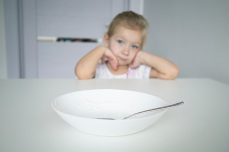 Child girl blonde on the table stands a dirty plate on a white tableの写真素材