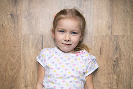Beautiful child girl in a T-shirt lies on a wooden floor. Top view, flat layの写真素材