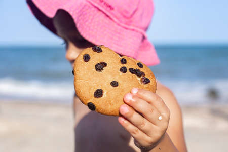 Child girl in panama hat holds cookies on the beachの写真素材