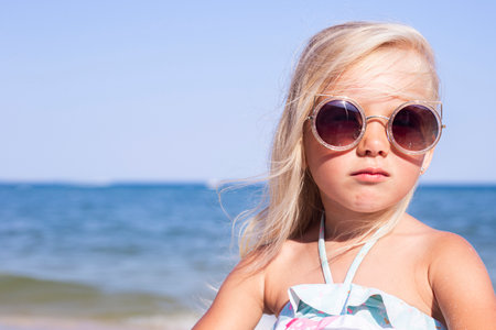 Beautiful child girl in sunglasses on the beach on a sunny dayの写真素材