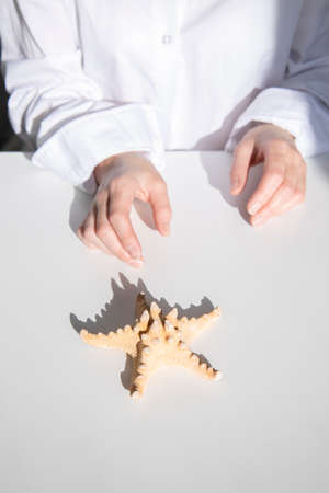 Female hands reach for a starfish on a white table. Top view, flat lay