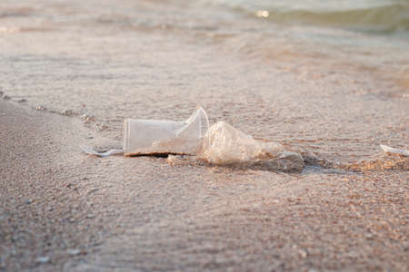 Plastic dishes and a plastic bag on the background of a sandy beach.の写真素材