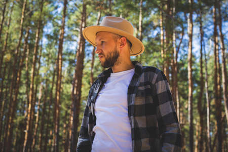 Man tourist in hat and plaid shirt in the woods.