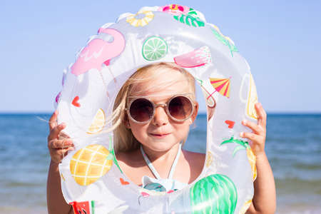 Smiling child girl in sunglasses looks through an inflatable circle on the beach
