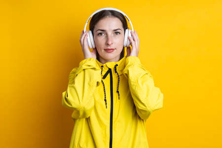 Young woman in headphones in a yellow jacket on a yellow background