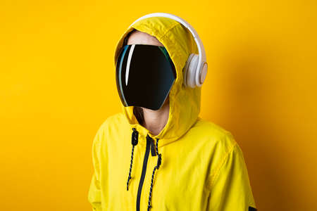 Young woman in cyberpunk glasses with headphones in a yellow jacket on a yellow background.の写真素材