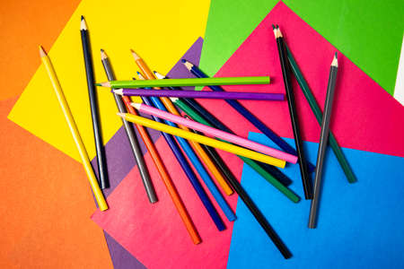 Many colored pencils lie on colored paper. Top view, flat lay.