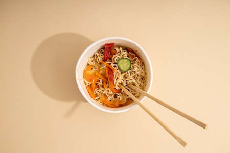Chinese noodles with vegetables in a paper bowl on a light background. Top view, flat lay.の写真素材