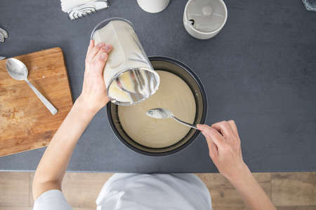 Woman pouring dough into baking dish. Top view, flat lay.