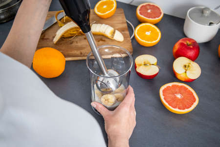 Woman using a hand blender to mix fresh fruits in the kitchen. Top view, flat lay.の写真素材