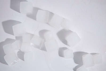 Ice cubes are scattered on a white background. Top view, flat lay.