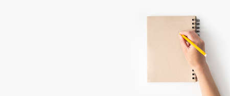 Female hand writes with a pencil on a notebook on a white background. Banner.の写真素材
