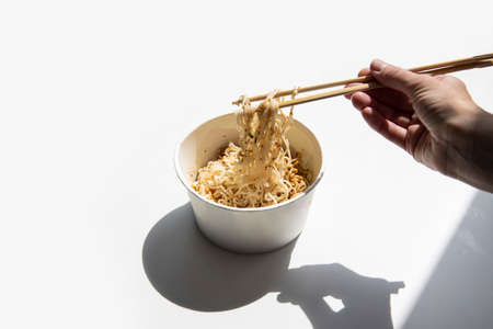 Female hands hold chinese chopsticks picking noodles in a cardboard bowl on a white background.の写真素材