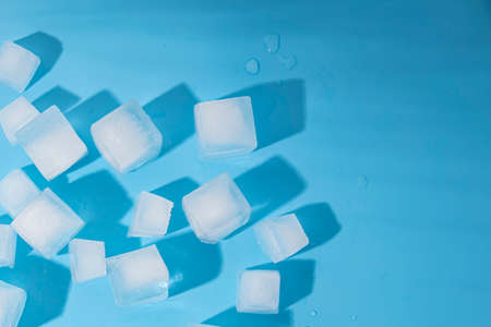 Many ice cubes on a blue background. Top view, flat lay.