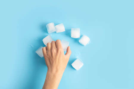 Female hand takes an ice cube on a blue background. Top view, flat lay.の写真素材