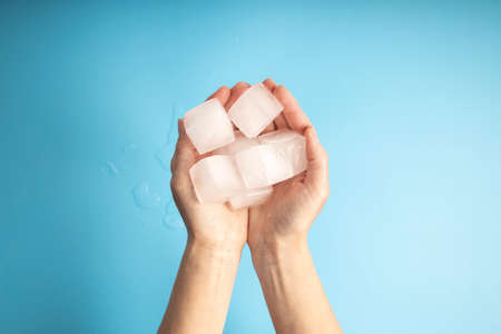 Woman's hand holding ice cubes on blue background. Top view, flat lay.の写真素材