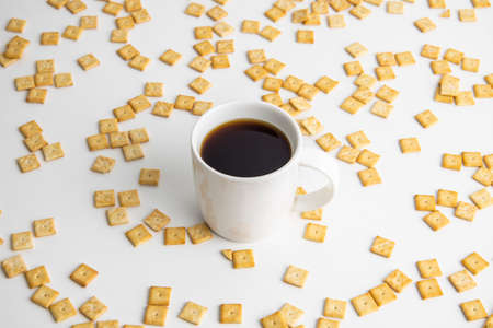 Coffee in a white cup on the background of a scattered crispy cracker on a white background.の写真素材