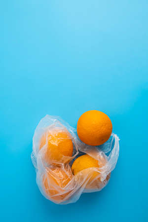 Fresh ripe oranges in a transparent plastic bag on a blue background. Top view, flat lay.の写真素材