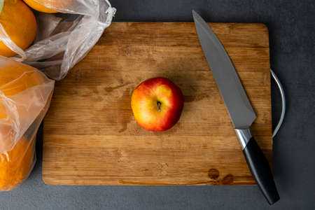 Red apple and knife lay on a wooden cutting board in the kitchen.Top view, flat lay.の写真素材