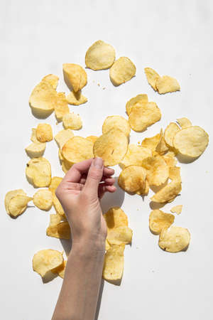 Woman's hand holding chips on a white background. Top view, flat lay.の写真素材