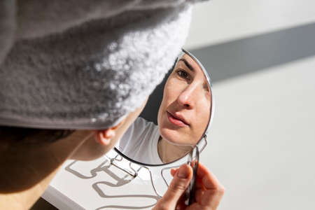 Young woman with a towel on her head applying morning makeup.